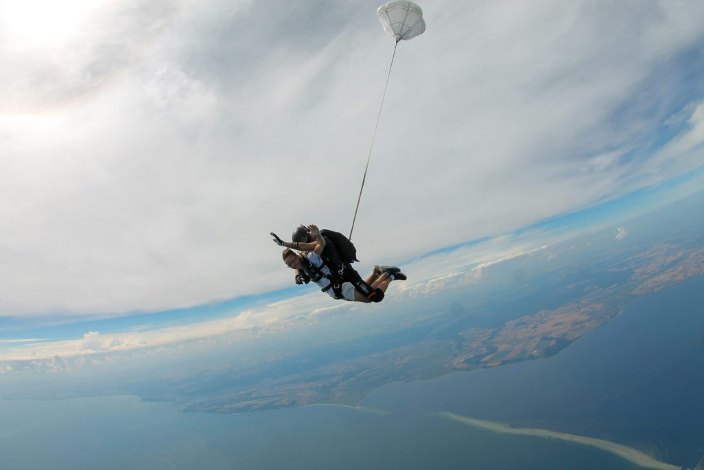 homme en veste noire et pantalon noir faisant du parachute sous des nuages ​​blancs et un ciel bleu pendant